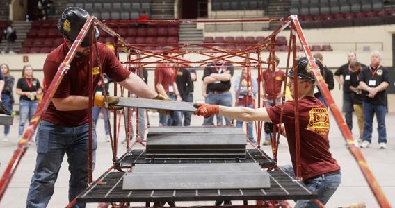 Two of the UMD steel bridge team students put weight on their bridge during the weight testing phase of the competition