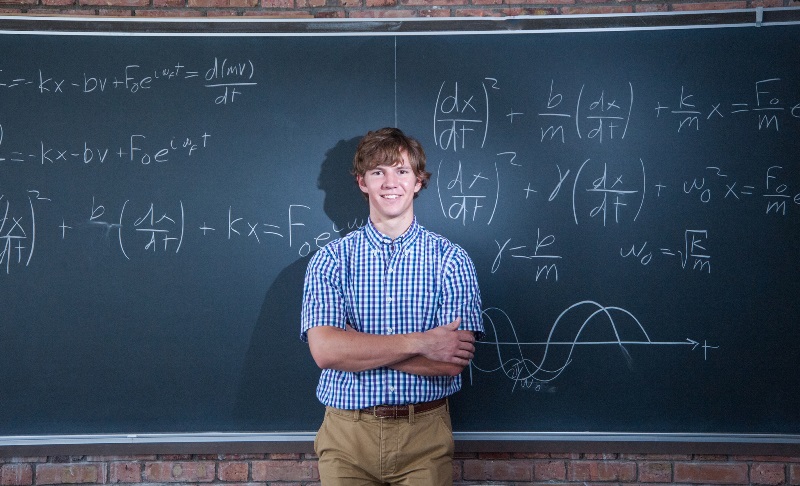 student infront of chalkboard with equations on the board